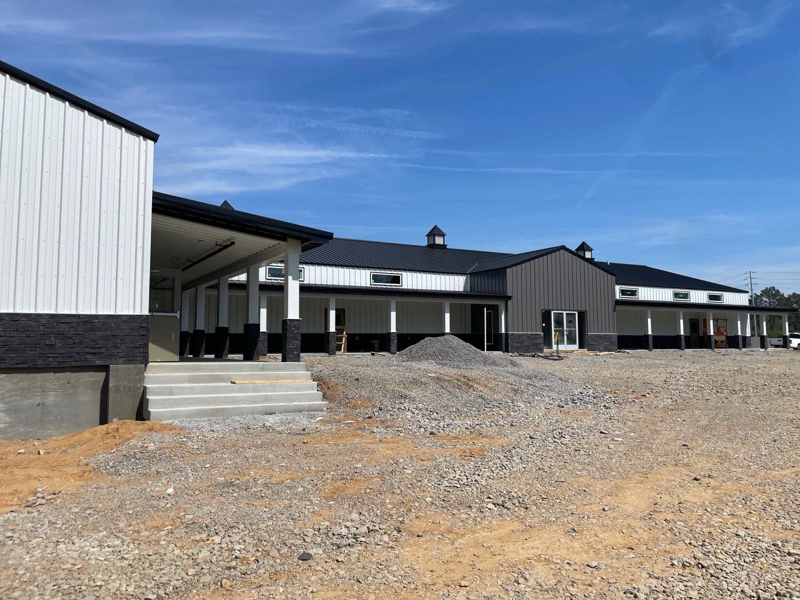 Long view of the completed front porch at Thompson's Station Hardware, showing timber columns, stone bases, finished concrete steps, and the full length of the storefront.