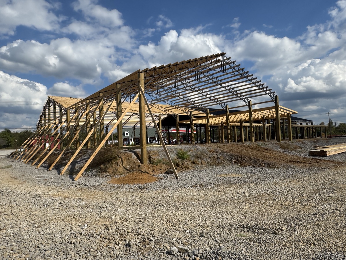 Inside view of Thompsons Station Hardware under construction in Franklin, TN, displaying the intricate network of steel trusses and wooden roof supports extending into the distance.
