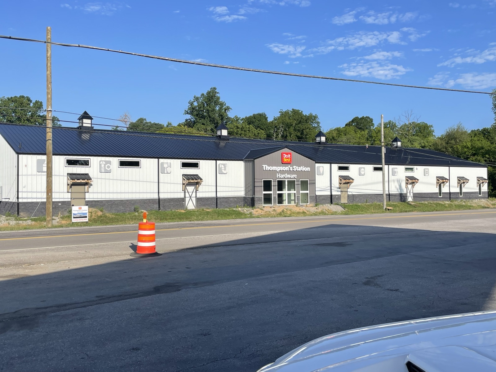 Wide view of the completed Thompson's Station Hardware exterior showing the full length of the building, finished siding, covered entry porches, and the Do it Best branding on the front gable.